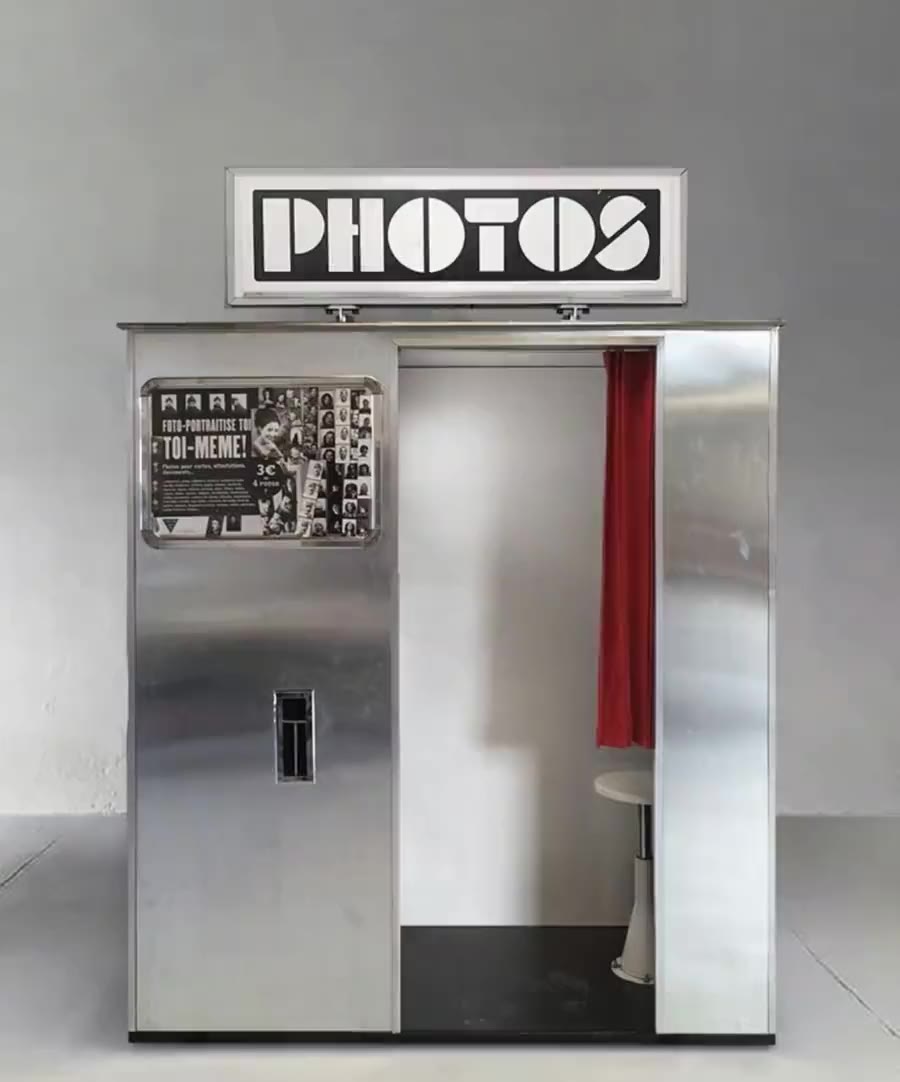 A vintage chrome photo booth with a red curtain, standing intact
